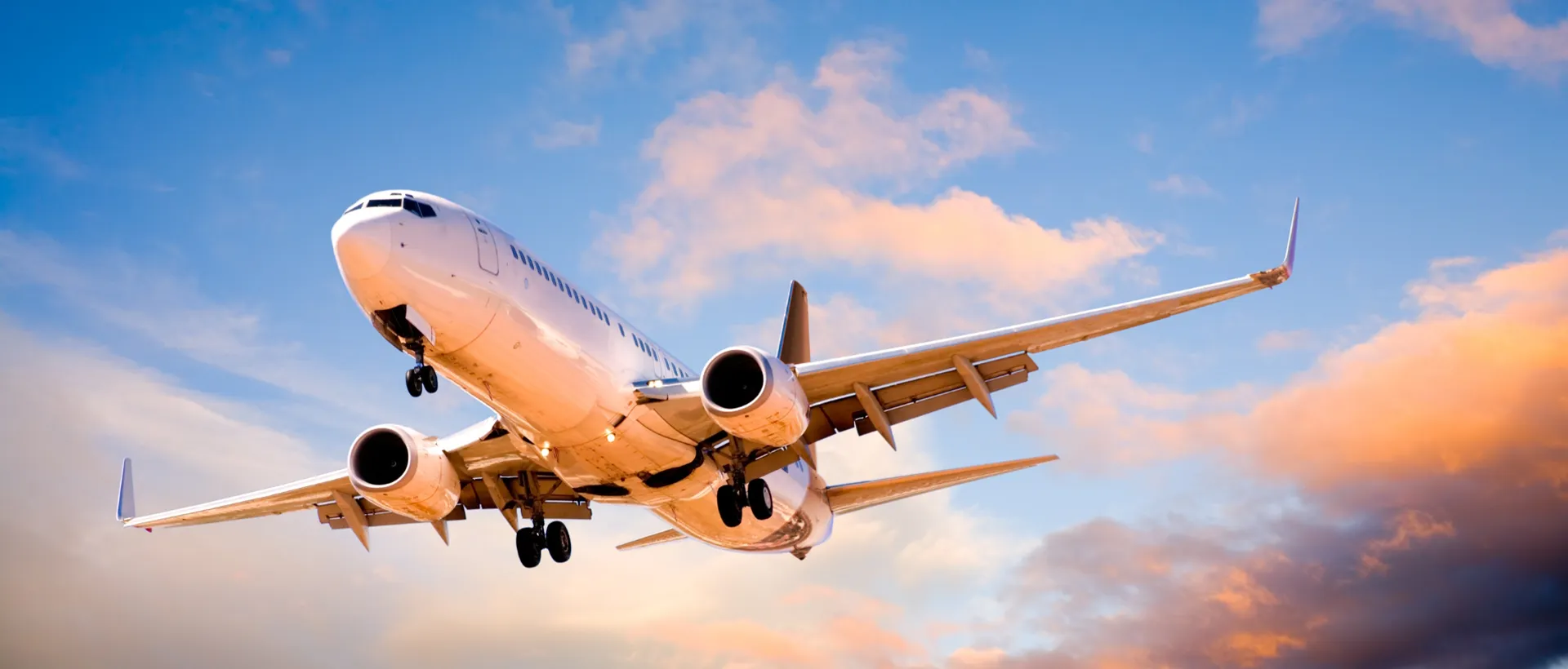 • A commercial airliner flying through an orange sunset sky, viewed from below.